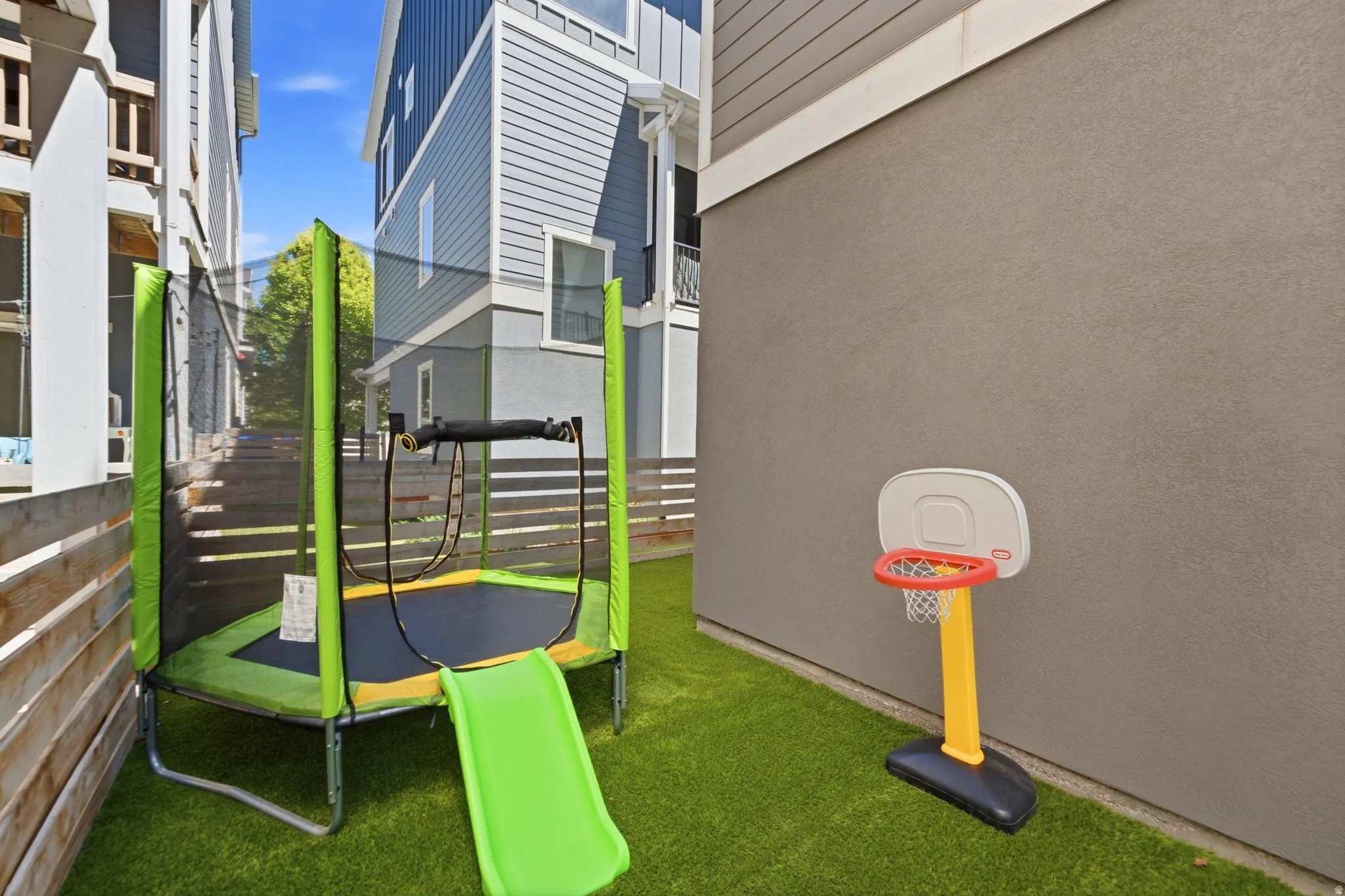 Compact outdoor space featuring artificial turf, a wood slat fence, and a stucco exterior