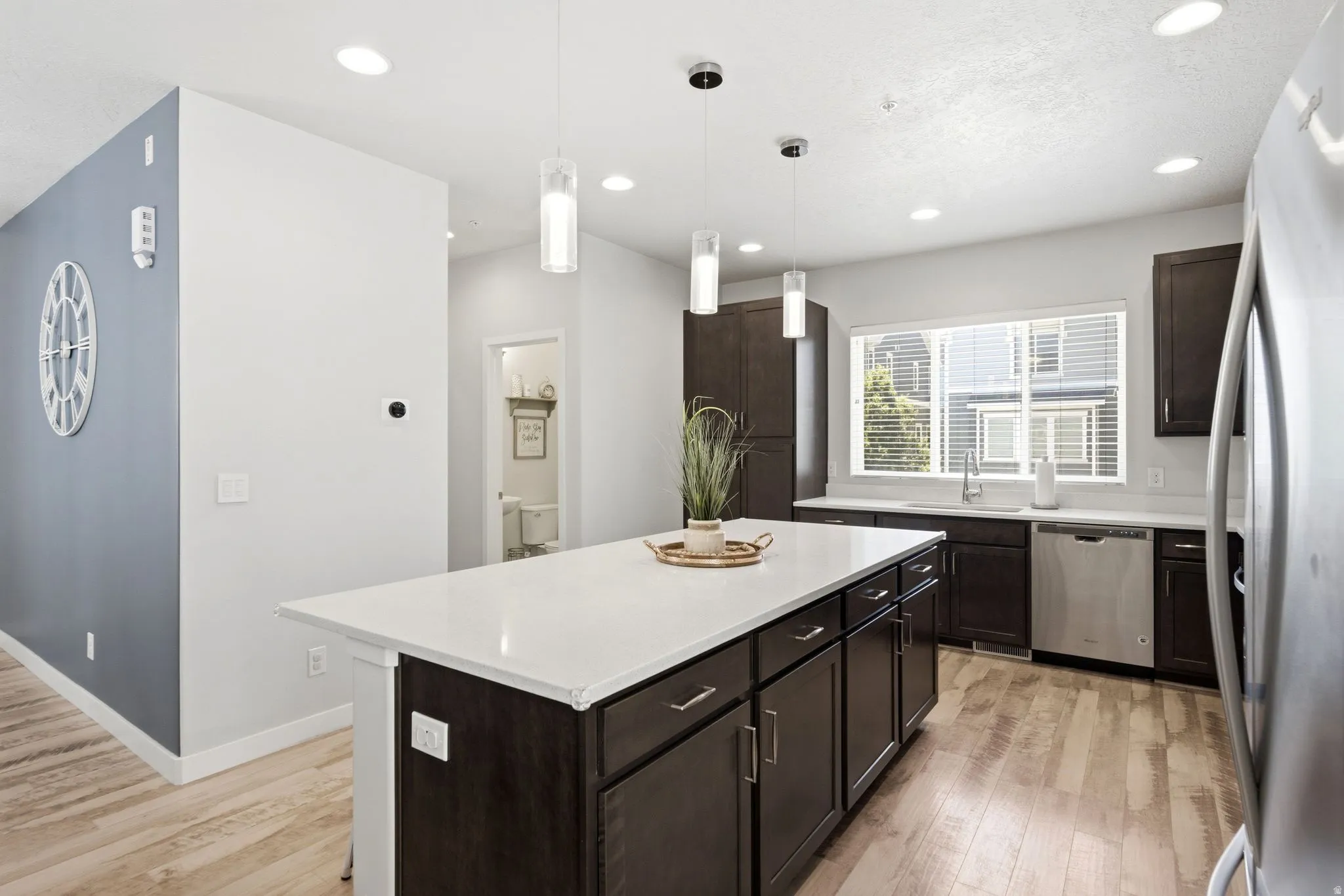 Kitchen featuring a large central island with a white countertop, dark wood-finish cabinetry, stainless steel appliances, and wood-finish flooring