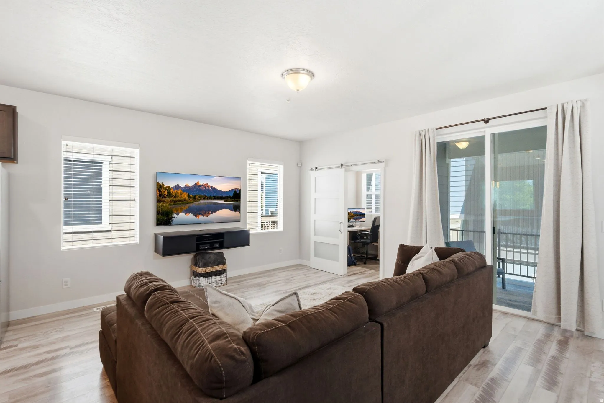 Open-concept living area featuring wood-finish flooring, a contemporary sliding glass door to the exterior, and a modern barn door entry to an additional room