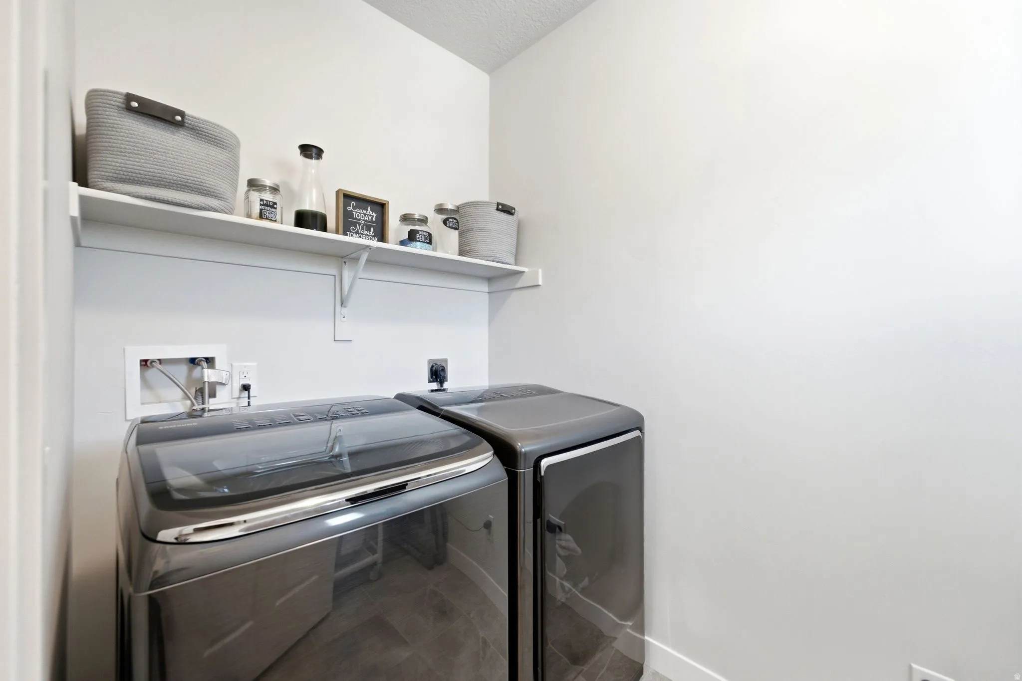 Dedicated laundry area featuring a floating white shelf, light gray walls, and dark tile flooring