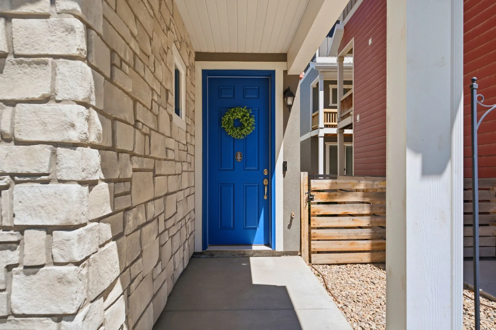 Stone veneer exterior with a vibrant blue entry door, featuring an overhead porch light and a white support column