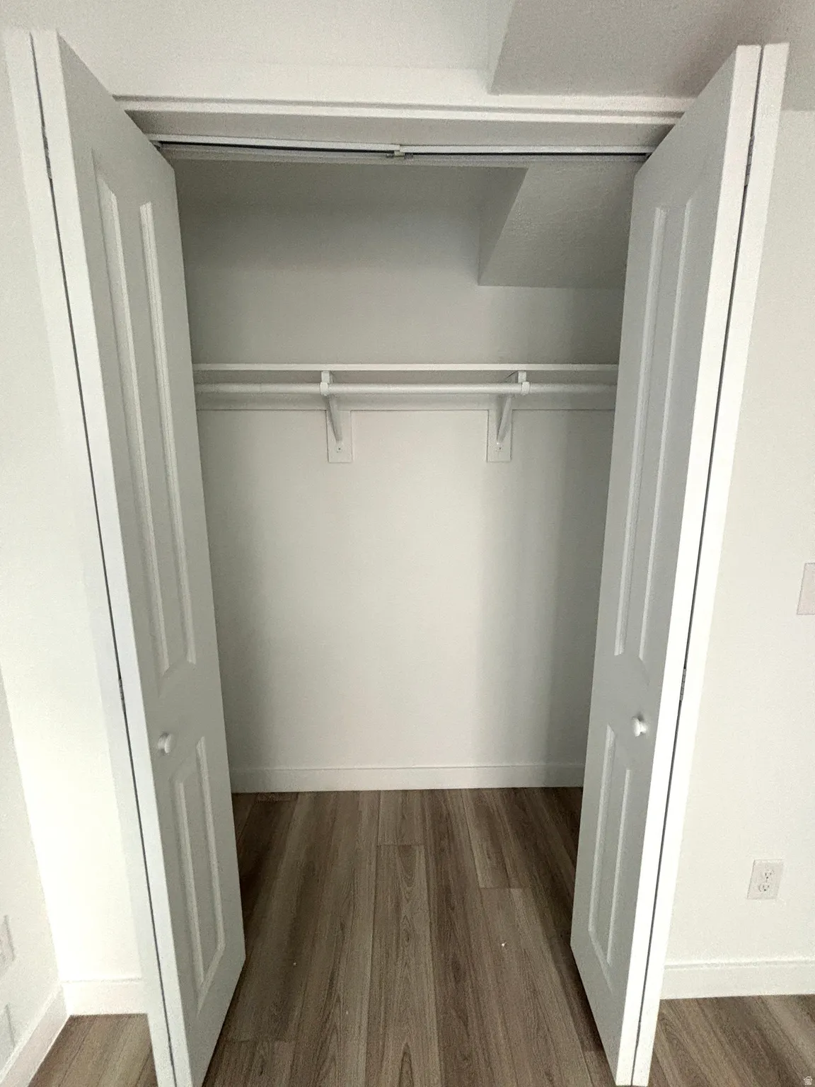 Interior closet featuring bi-fold doors, wood-finish flooring, white walls, and built-in shelving with hanging rods