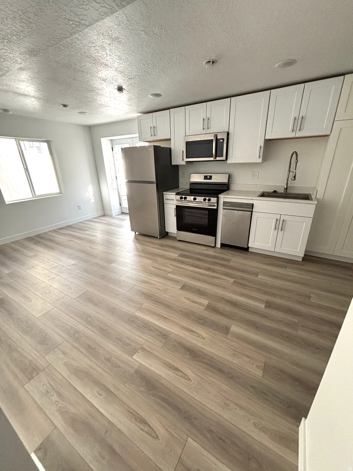 Open-concept living space featuring wood-finish flooring, white cabinetry, stainless steel appliances, and recessed lighting