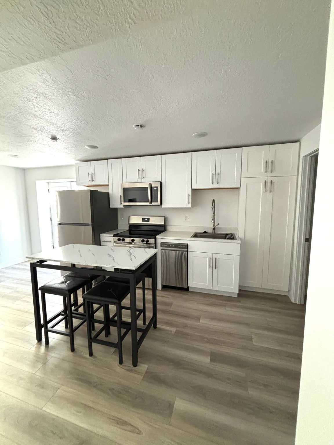 Contemporary kitchen featuring white cabinetry, stainless steel appliances, wood-finish flooring, and a stone-finish countertop