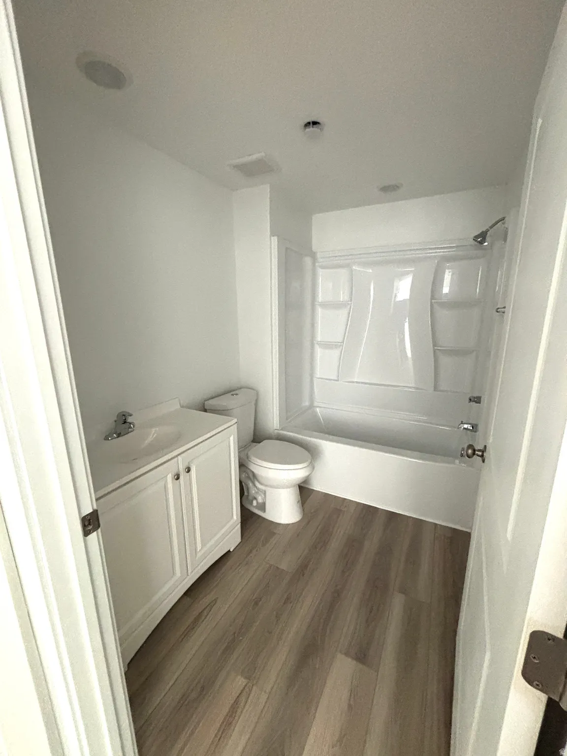 Bathroom featuring wood-finish flooring, a white vanity with integrated sink, a commode, and a bathtub with shower fixture