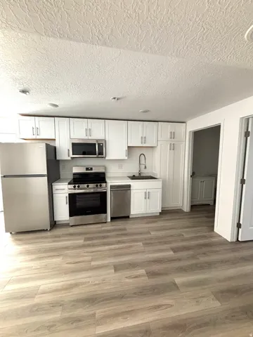Open-concept kitchen featuring wood-finish flooring, white cabinetry, stainless steel appliances, and a white subway tile backsplash