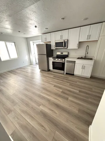Open-concept living space featuring wood-finish flooring, white cabinetry, stainless steel appliances, and recessed lighting