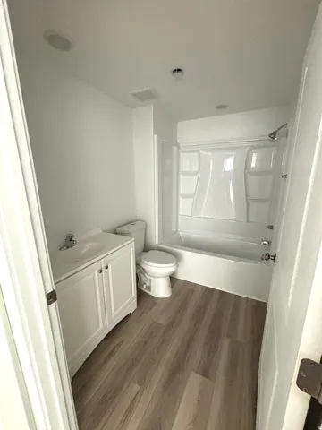 Bathroom featuring wood-finish flooring, a white vanity with integrated sink, a commode, and a bathtub with shower fixture
