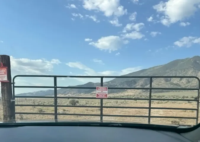 Expansive undeveloped land featuring a metal gate entrance and a wood post with a sign