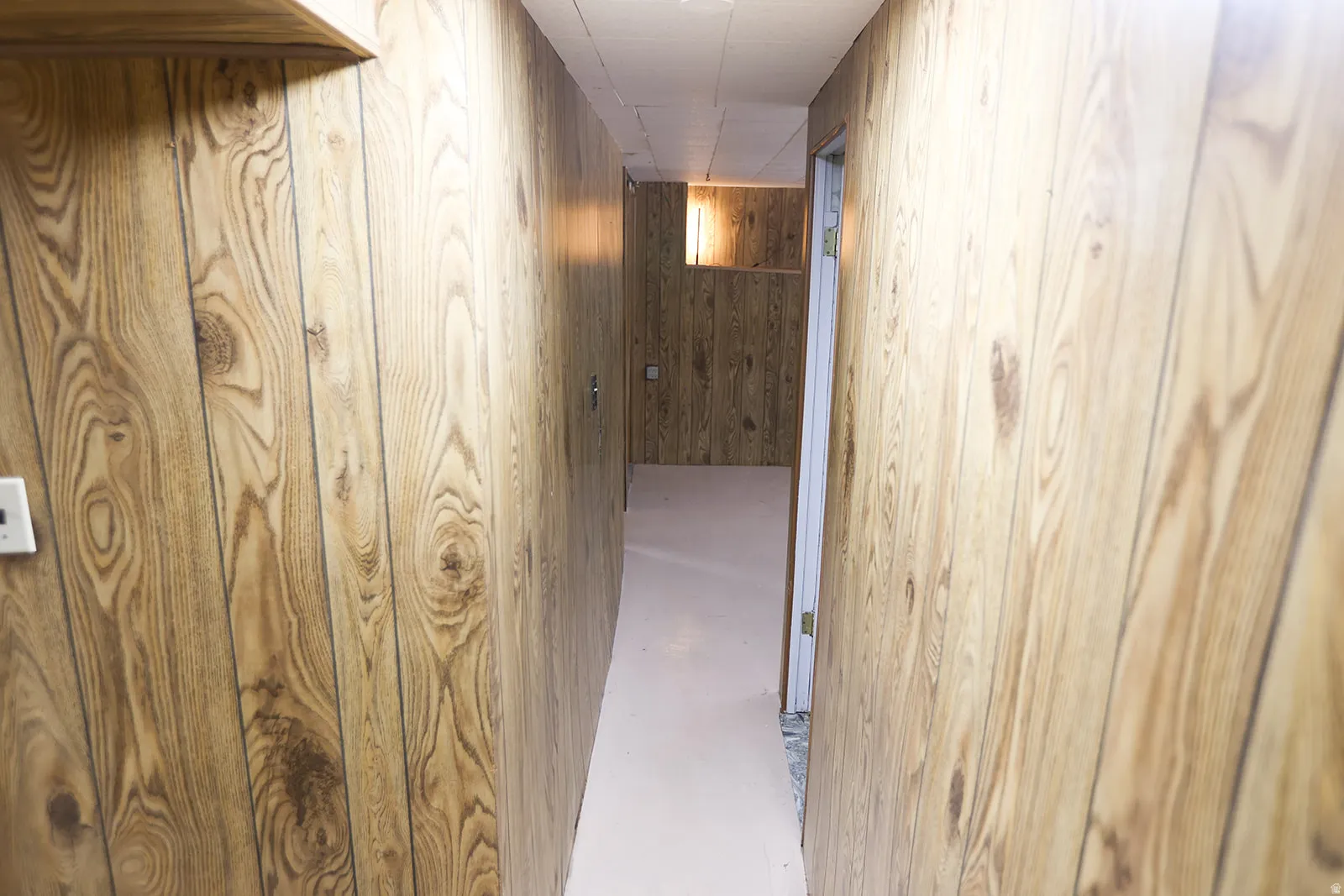 Hallway featuring wood-finish paneling, overhead lighting, and a neutral-toned floor