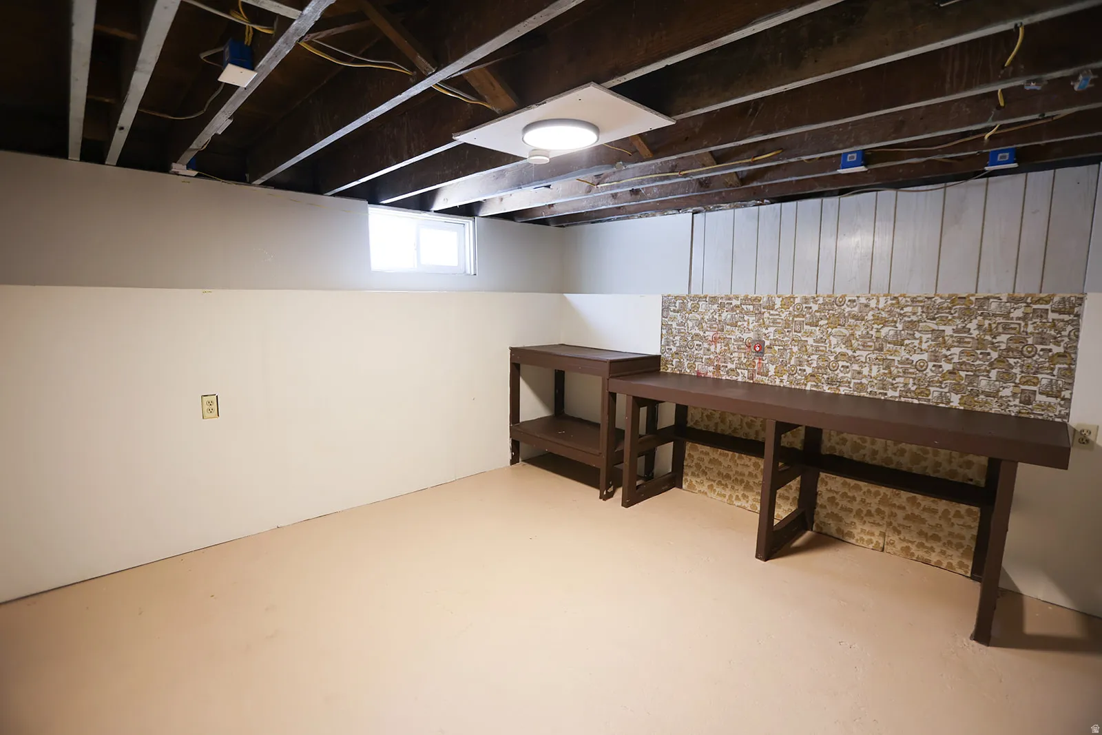 Basement space featuring exposed ceiling joists, light-toned painted concrete flooring, and built-in workbench