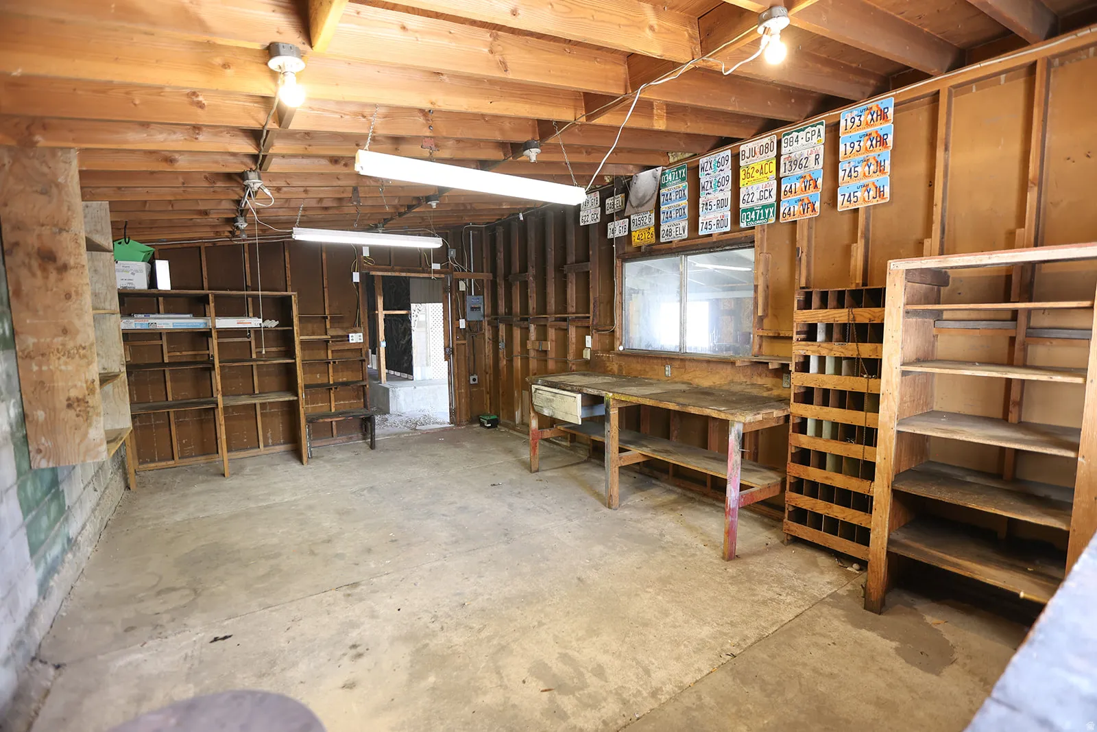 Enclosed workshop with ample storage, concrete flooring, exposed wood beam ceiling and wall framing