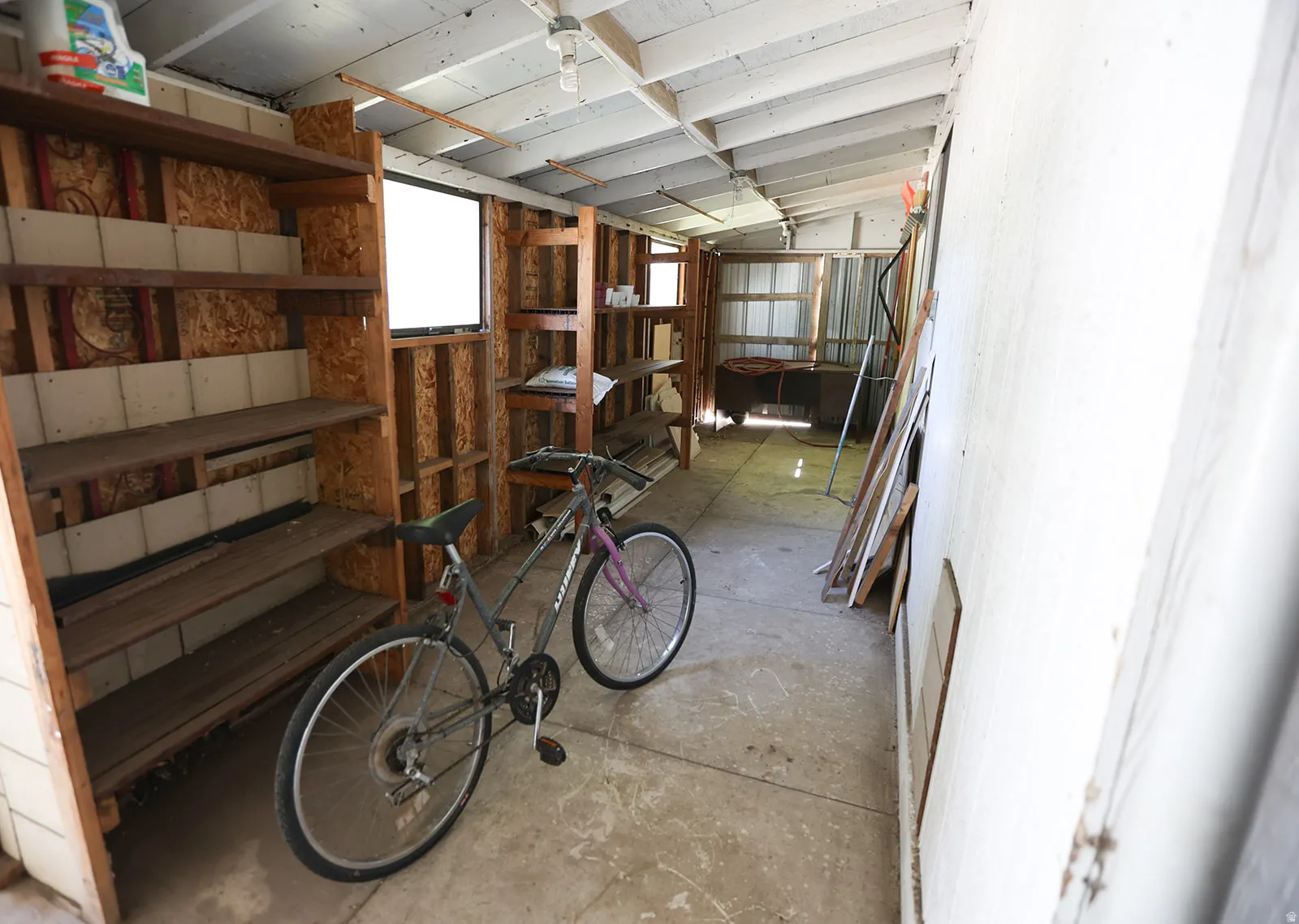 Spacious utility structure featuring a concrete floor, exposed wood beam ceiling, and built-in wood shelving