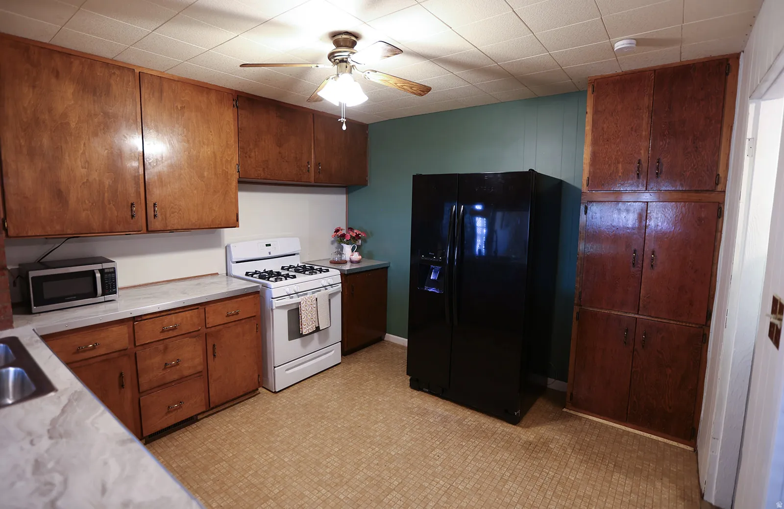 Kitchen featuring extensive wood cabinetry, a white gas range, a black side-by-side refrigerator, and patterned vinyl flooring