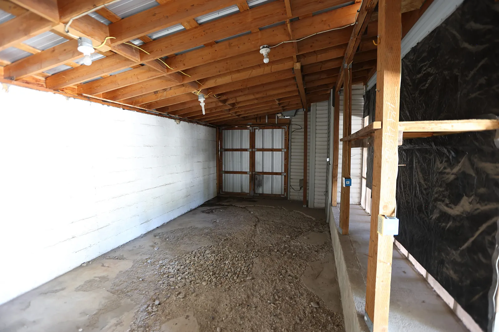 Sheltered outdoor space featuring a wood-beam ceiling, corrugated metal roofing, exposed wood framing, and integrated lighting fixtures