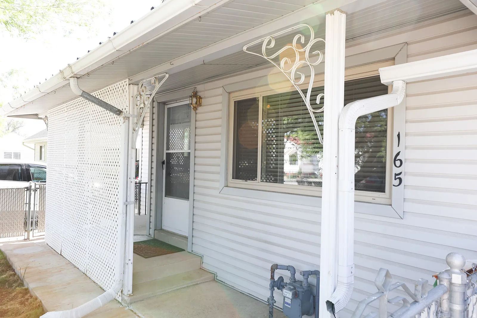Front entry featuring white vinyl siding, an overhead soffit, and decorative metal support brackets