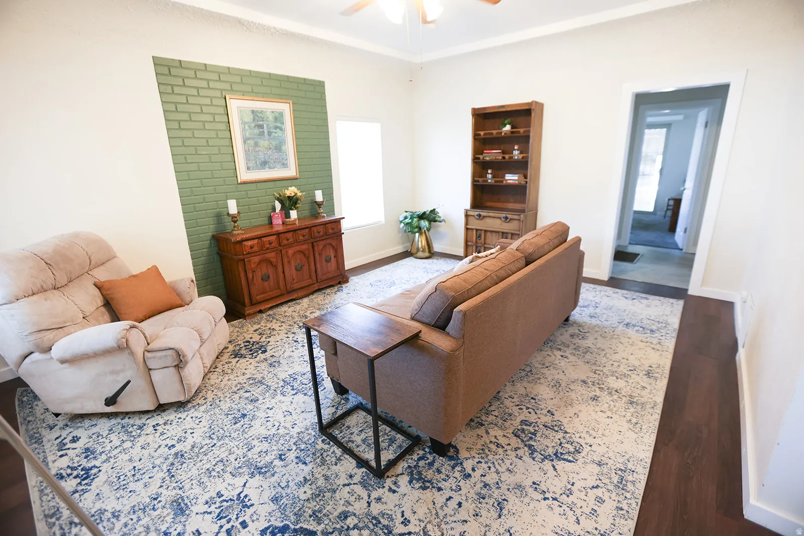 Living area featuring a distinctive green brick accent wall, wood-finish flooring, and a ceiling fan