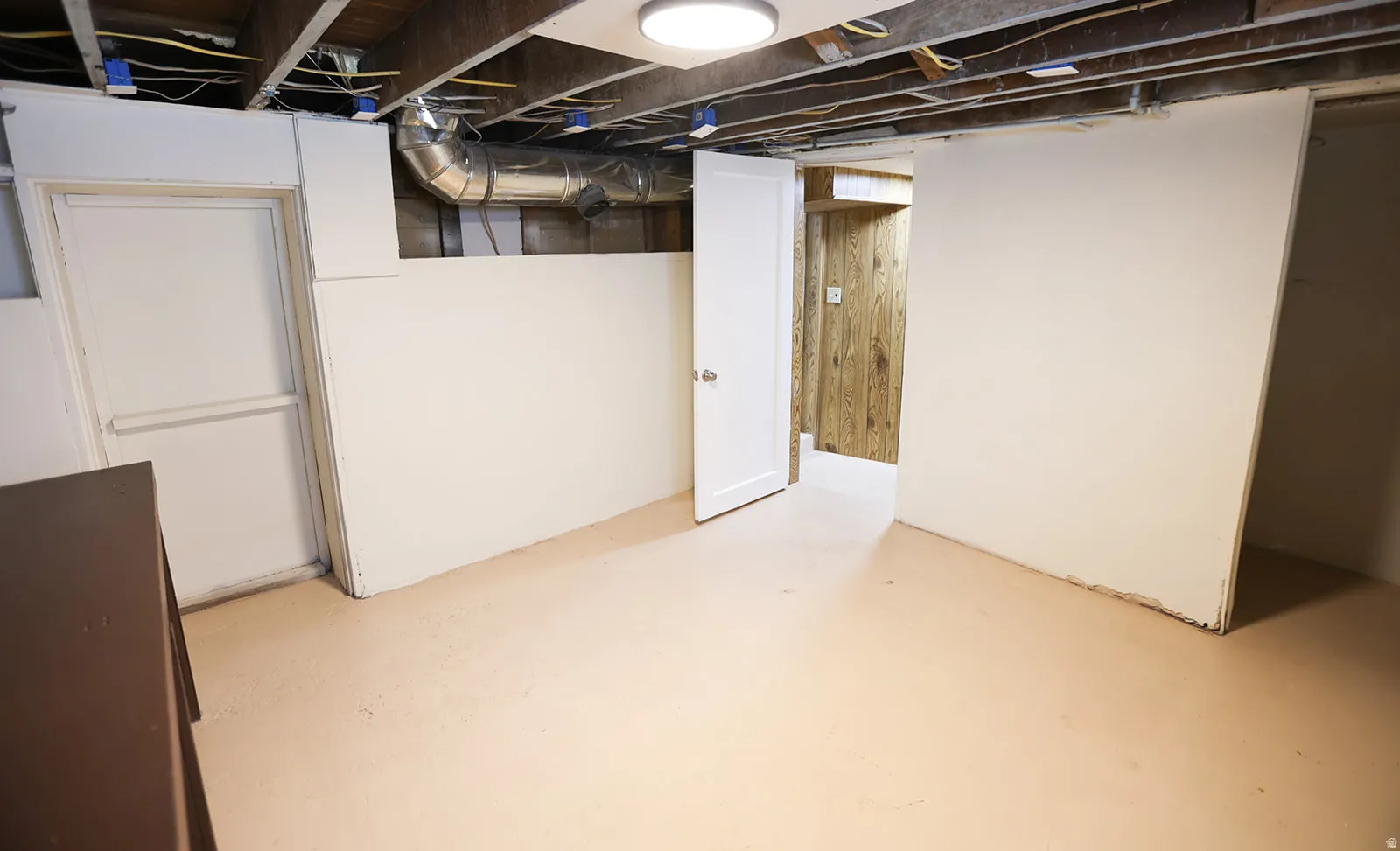 Unfinished basement space featuring exposed ceiling joists and ductwork, painted concrete flooring, and a white interior door