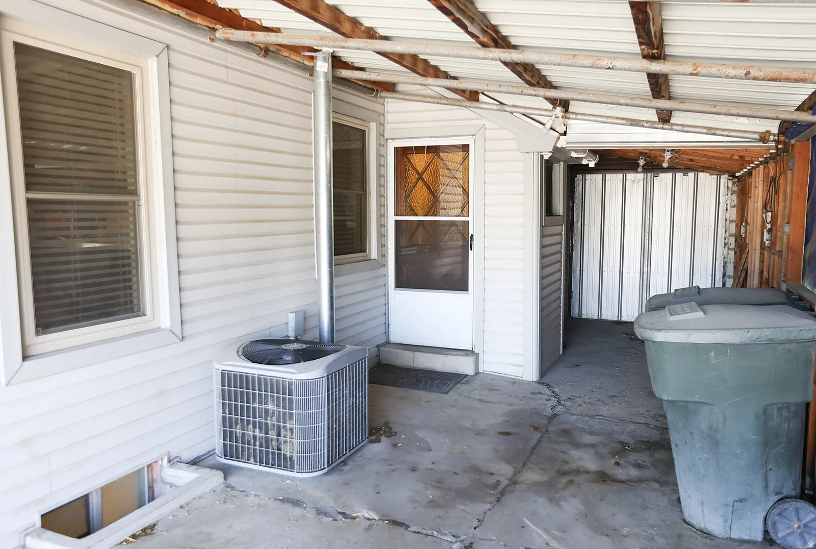 Covered exterior walkway featuring a white vinyl-sided wall, a security door with decorative glass, and dual pane windows