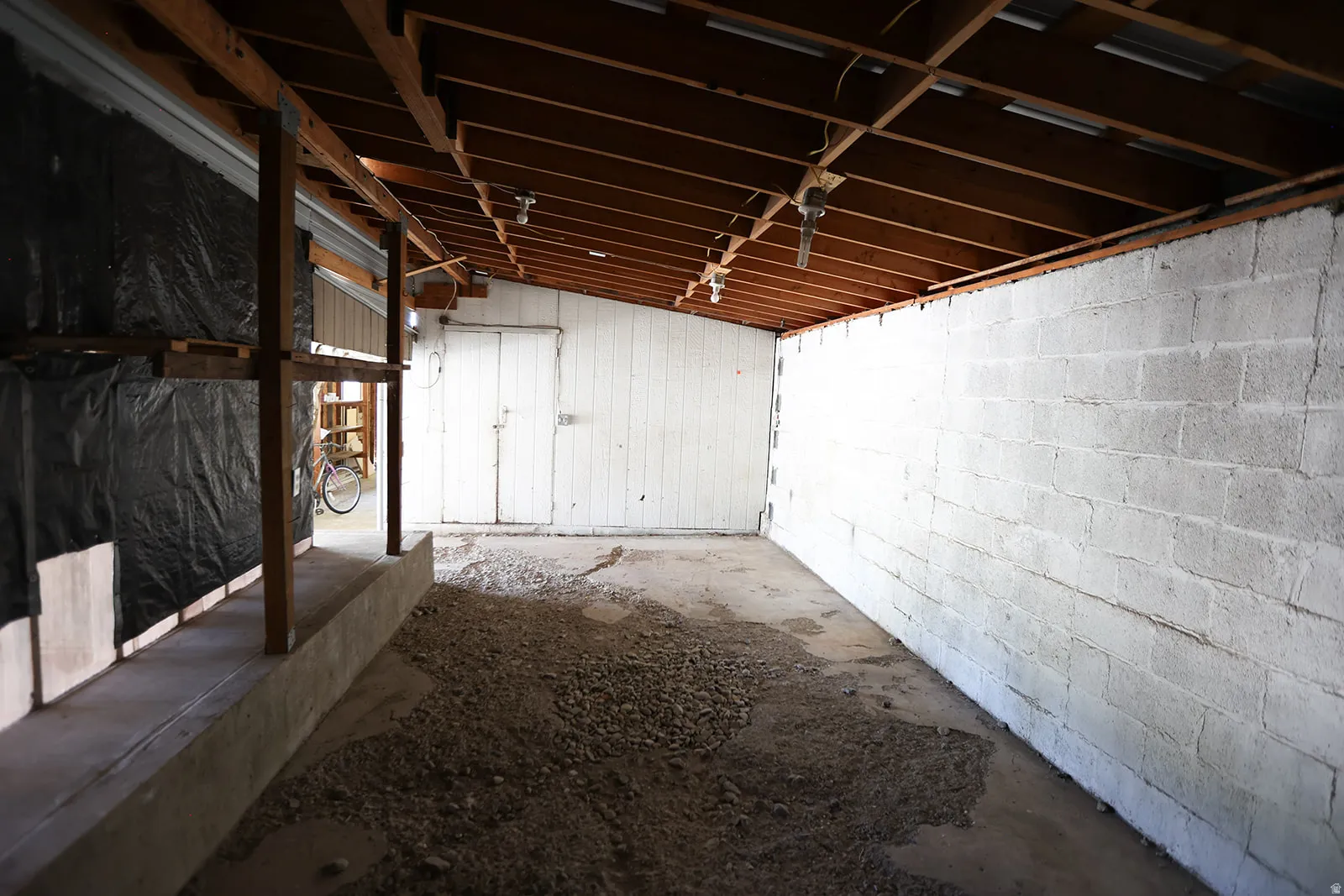 Exposed wood beam ceiling structure with concrete block walls and a partial gravel floor