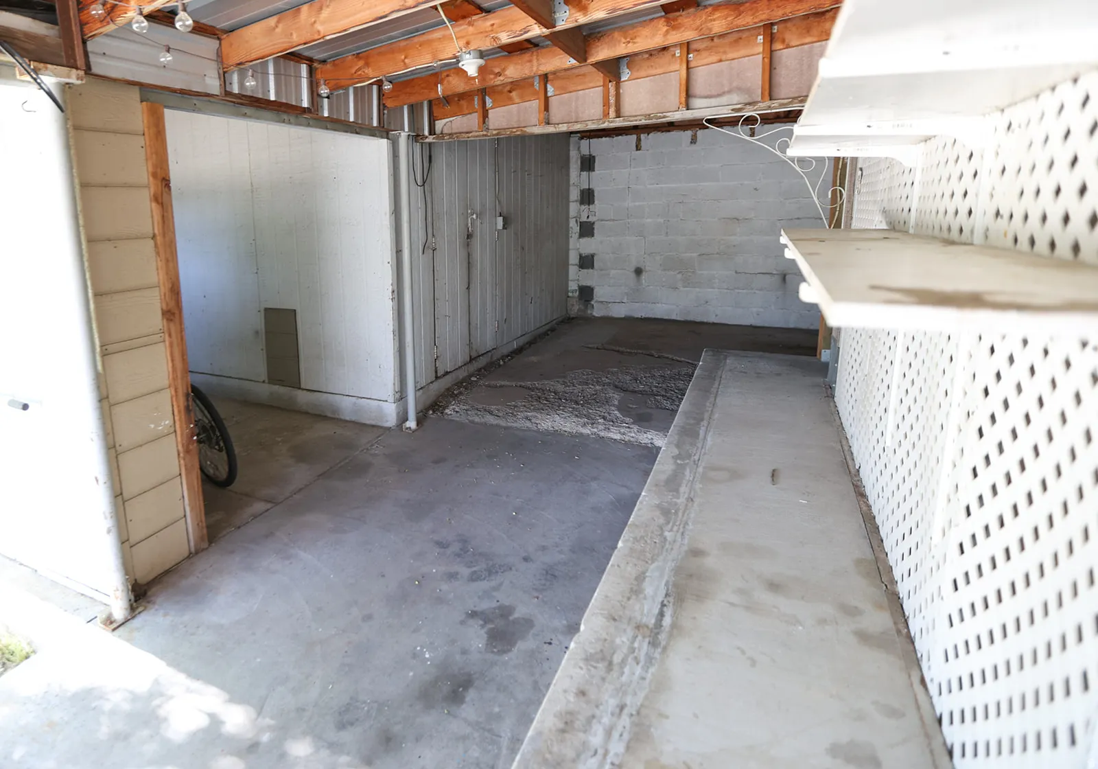 Covered outdoor area featuring a concrete floor, exposed wood ceiling beams, and a white lattice privacy wall with built-in shelving