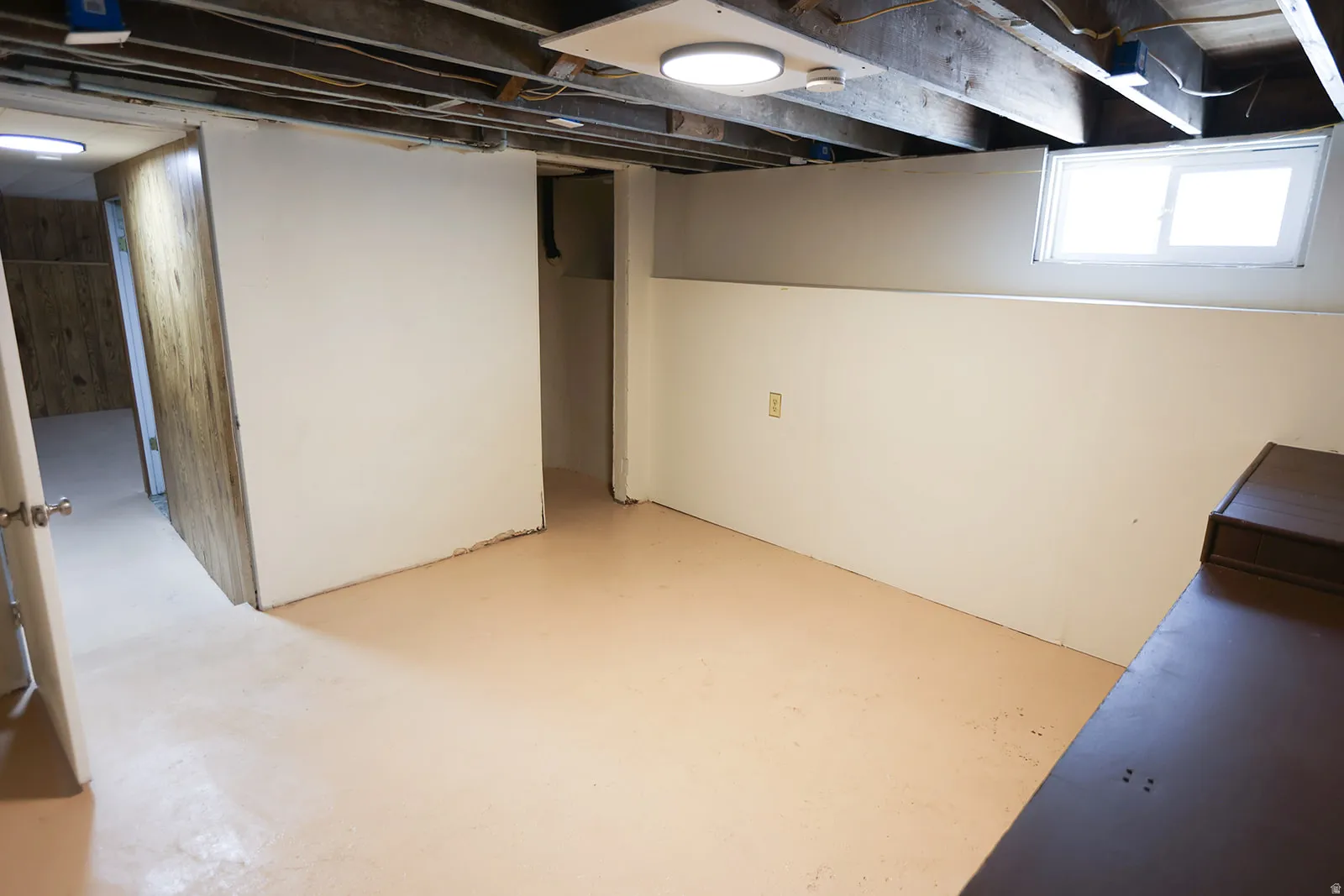 Finished lower level space featuring exposed ceiling joists, white paneled walls, and light-colored flooring