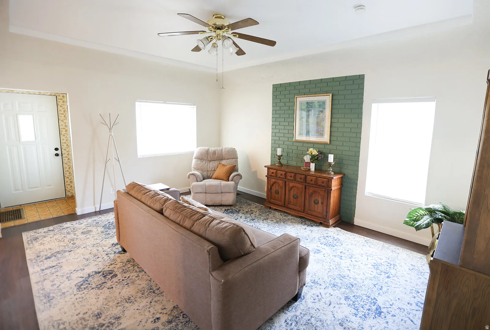 Spacious room featuring dark wood-finish flooring, a ceiling fan with integrated lighting, and multiple windows