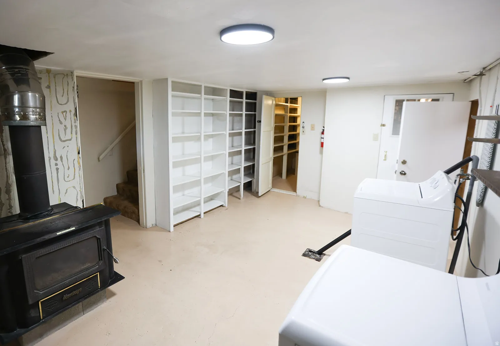 Finished lower level featuring a wood-burning stove, built-in shelving, a storage pantry with additional shelving, a utility door, and a staircase