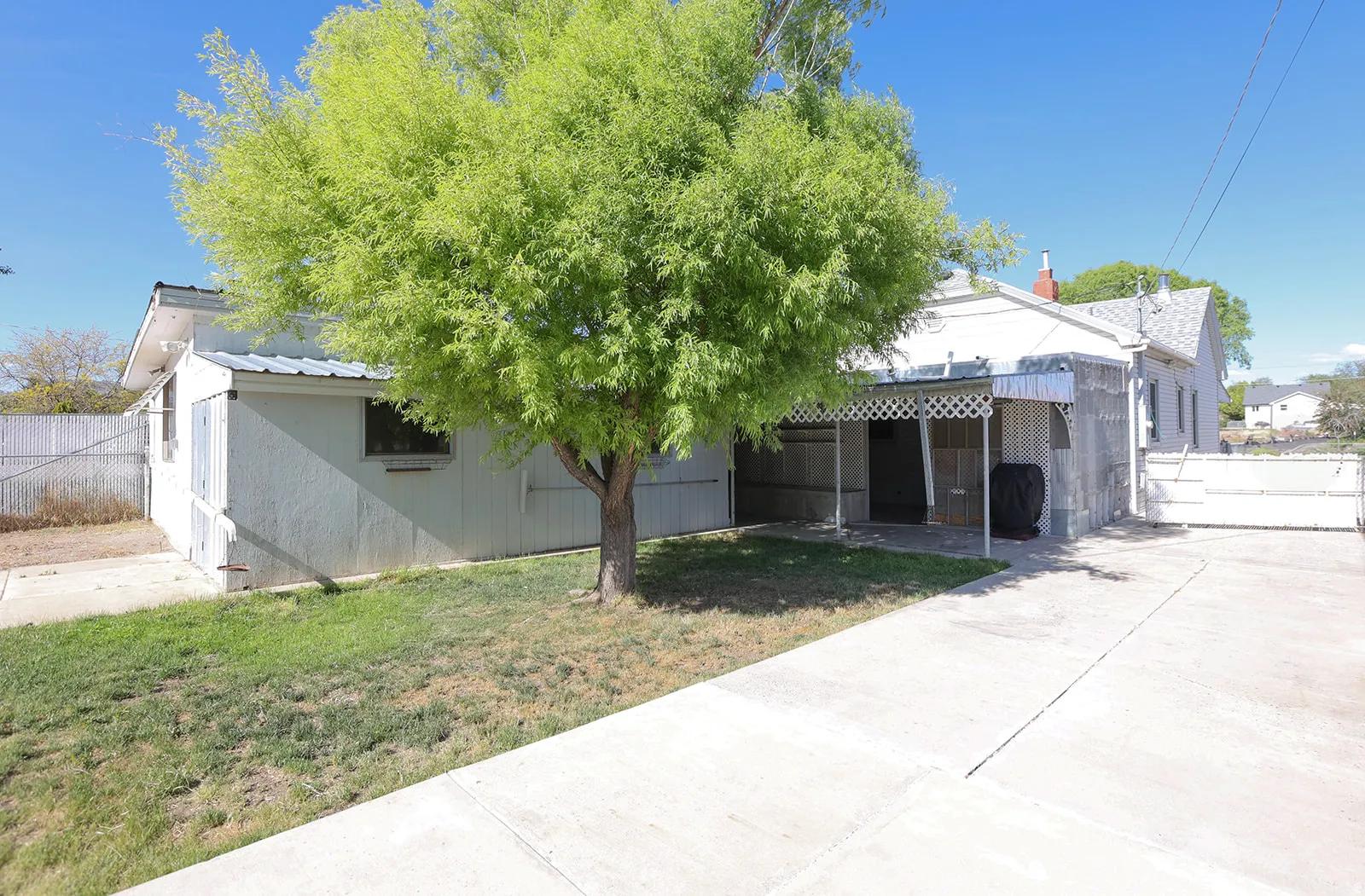 Concrete driveway leading to a covered carport with decorative lattice detailing