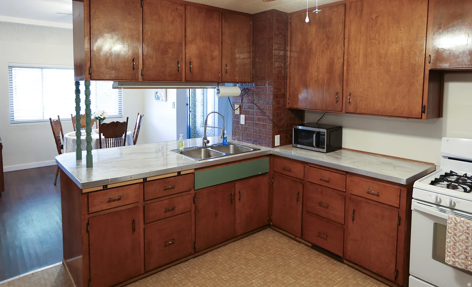 Kitchen featuring wood-finish cabinetry, a double basin stainless steel sink, a gas range, and light-toned countertops