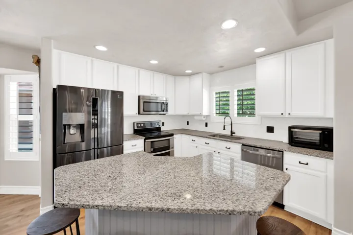 Kitchen featuring a large island with a light speckled countertop, white cabinetry, a black appliance suite, recessed lighting, and a white tile backsplash