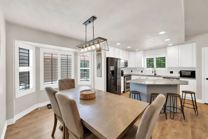 Open-concept kitchen and dining area featuring wood-finish flooring, white cabinetry, granite-finish countertops, and stainless steel appliances, upgraded fixtures.