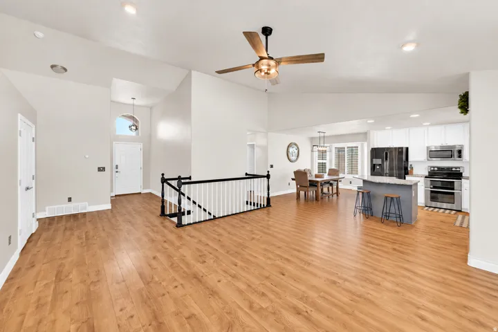 Expansive living area with high vaulted ceilings, wood-finish flooring, and a ceiling fan with integrated lighting