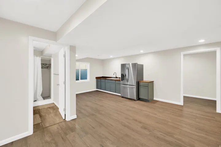 Open-concept room featuring wood-finish flooring, recessed lighting, and a kitchen area with gray cabinetry, a dark countertop, and a stainless steel refrigerator