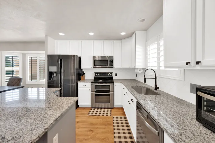 Modern kitchen featuring white cabinetry, granite countertops, wood-finish flooring, stainless steel appliances, and a tile backsplash