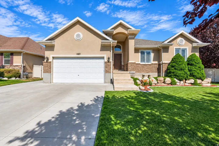 Stucco exterior with brick accents, concrete driveway, attached two-car garage, and a manicured lawn with mature landscaping