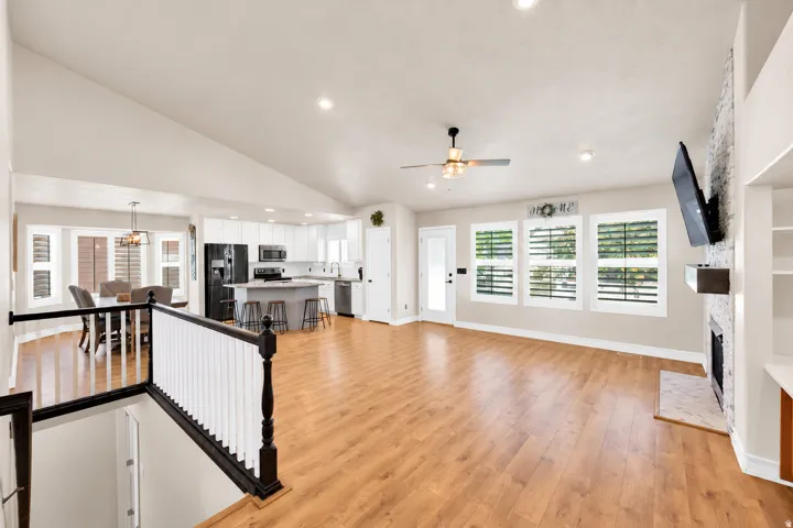 Open-concept living space featuring wood-finish flooring, a white brick fireplace with a wood mantle, and a kitchen with white cabinetry and an island