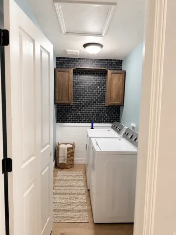 Laundry area featuring wood-finish flooring, white beadboard paneling, black subway tile, and wood cabinetry