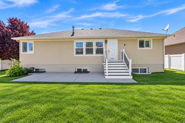 Expansive backyard with a manicured lawn, concrete patio, and white privacy fencing