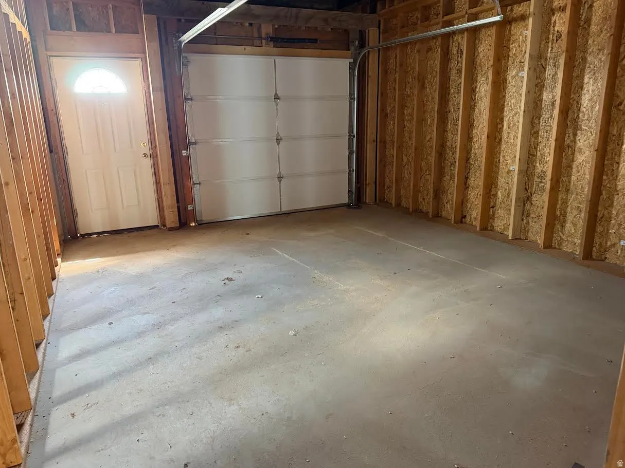 Spacious garage with a concrete floor, a white overhead door, and an insulated pedestrian door featuring an arched window