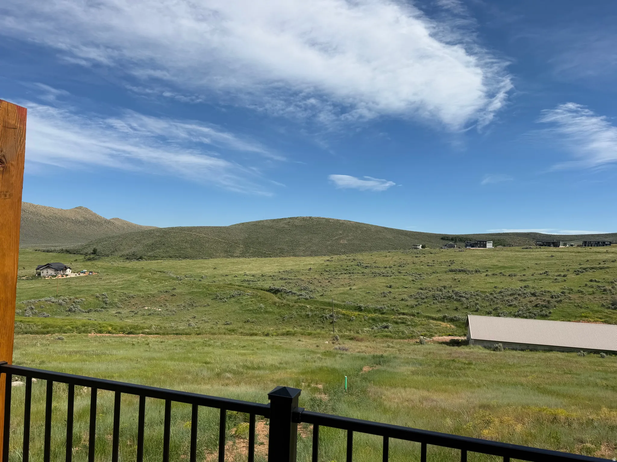 Expansive natural landscape featuring rolling hills and open fields, framed by a dark metal railing and a wood post