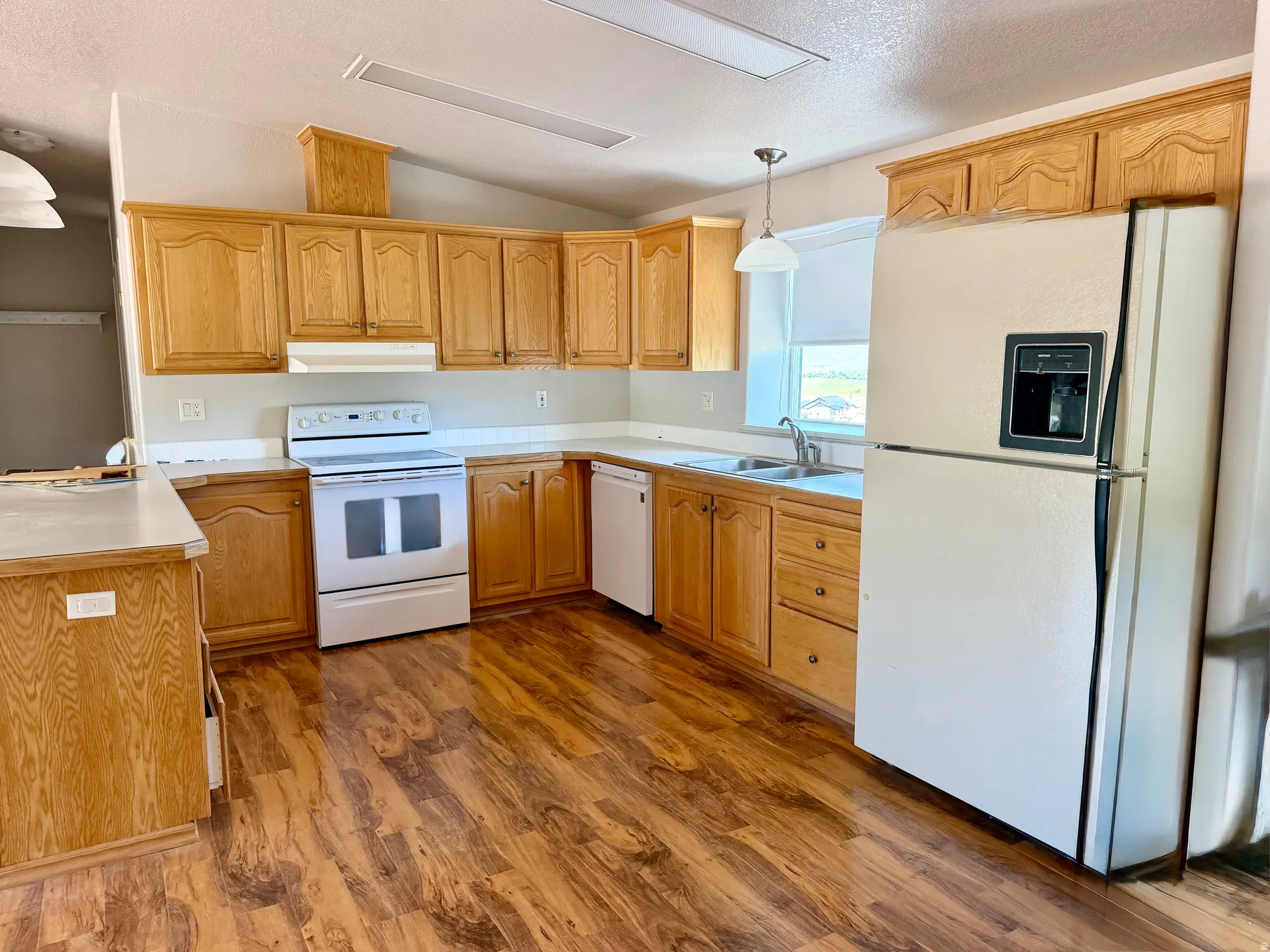 Kitchen featuring wood-finish flooring, light wood cabinetry, white countertops, a white electric range, and a white refrigerator with an ice and water dispenser