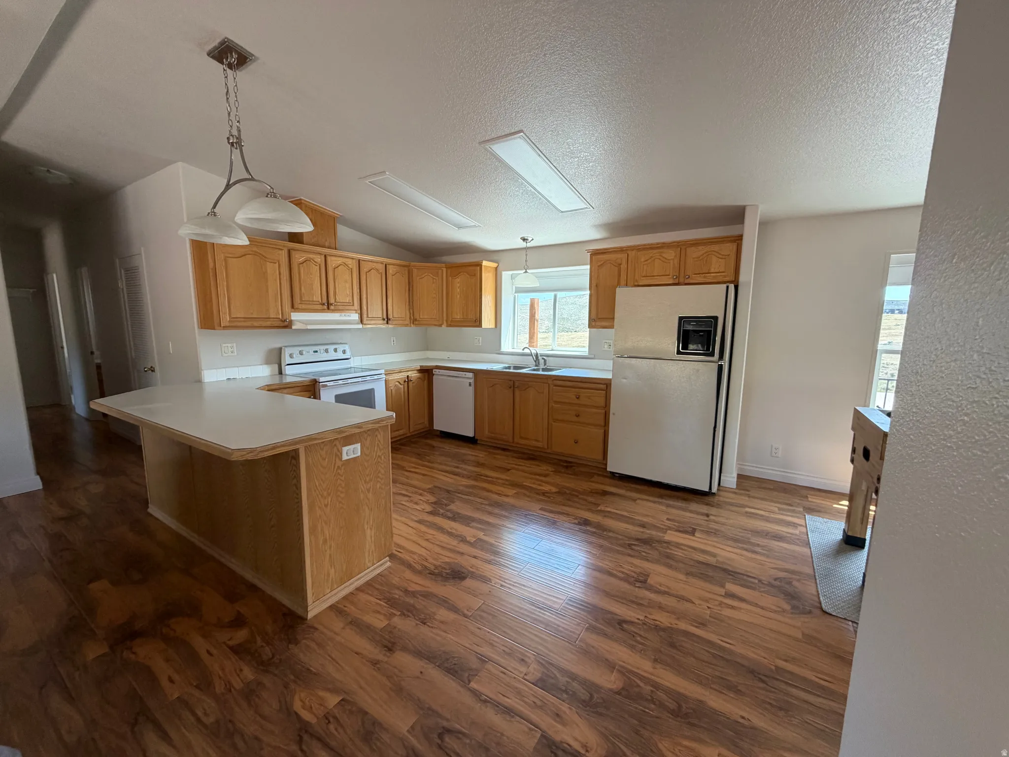 Spacious kitchen featuring wood-finish flooring, white countertops, ample wood cabinetry, and a central island with integrated power outlets