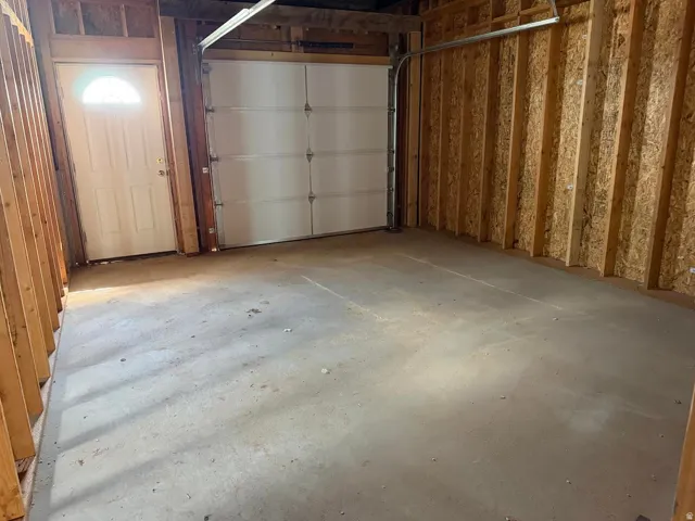 Spacious garage with a concrete floor, a white overhead door, and an insulated pedestrian door featuring an arched window