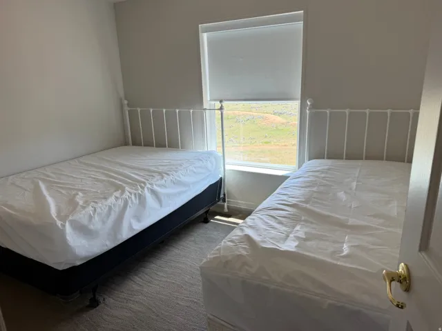 Bedroom featuring a window with roller shade, neutral wall paint, and textured carpet flooring