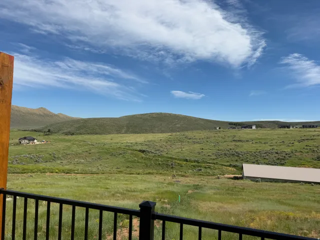 Expansive natural landscape featuring rolling hills and open fields, framed by a dark metal railing and a wood post