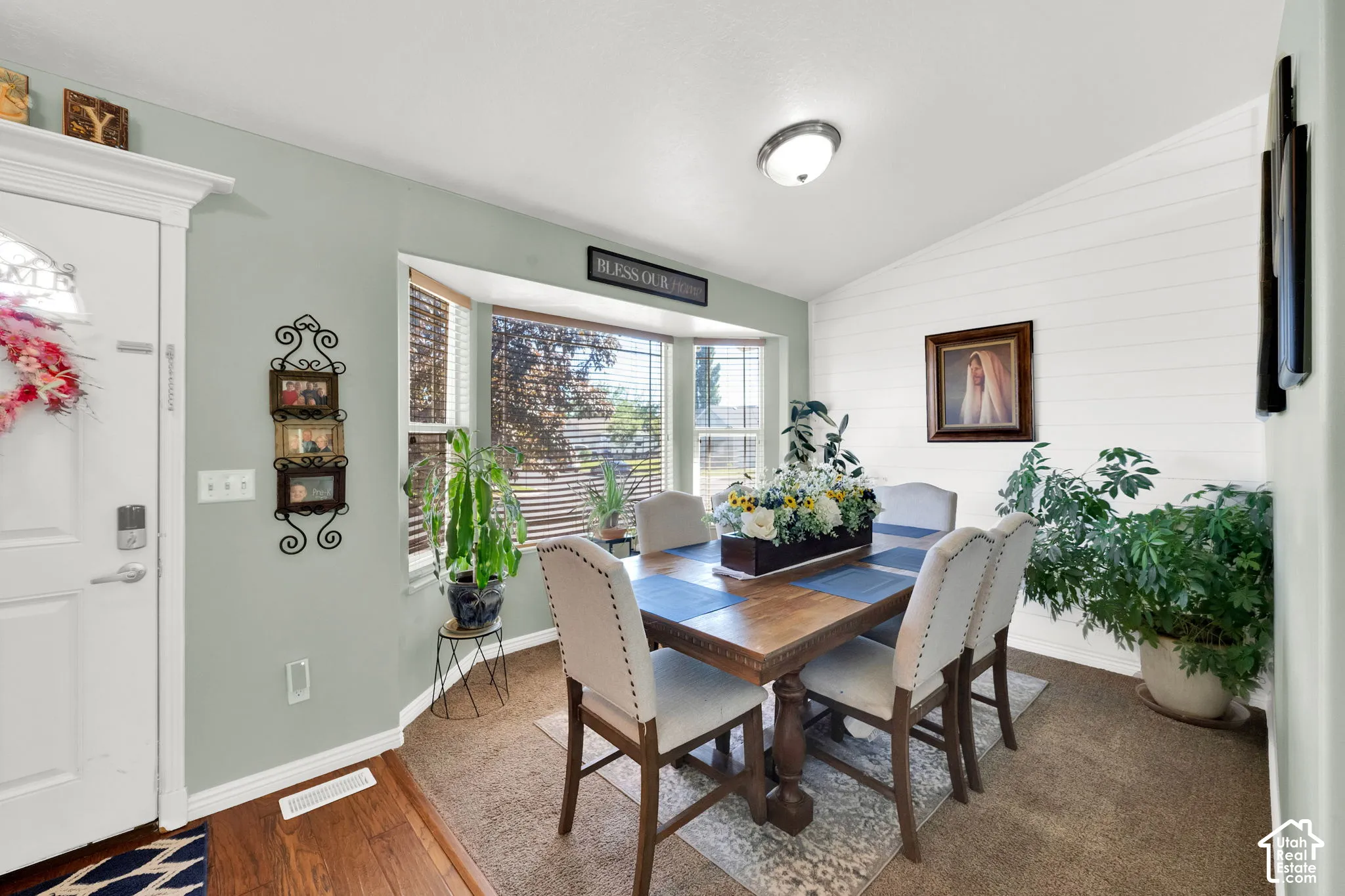 Dining area featuring a bay window with blinds, a wood-finish dining table, and a white shiplap accent wall