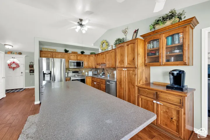 Kitchen featuring wood-finish flooring, a large island with a stone-finish countertop, wood cabinetry, stainless steel appliances, and vaulted ceilings
