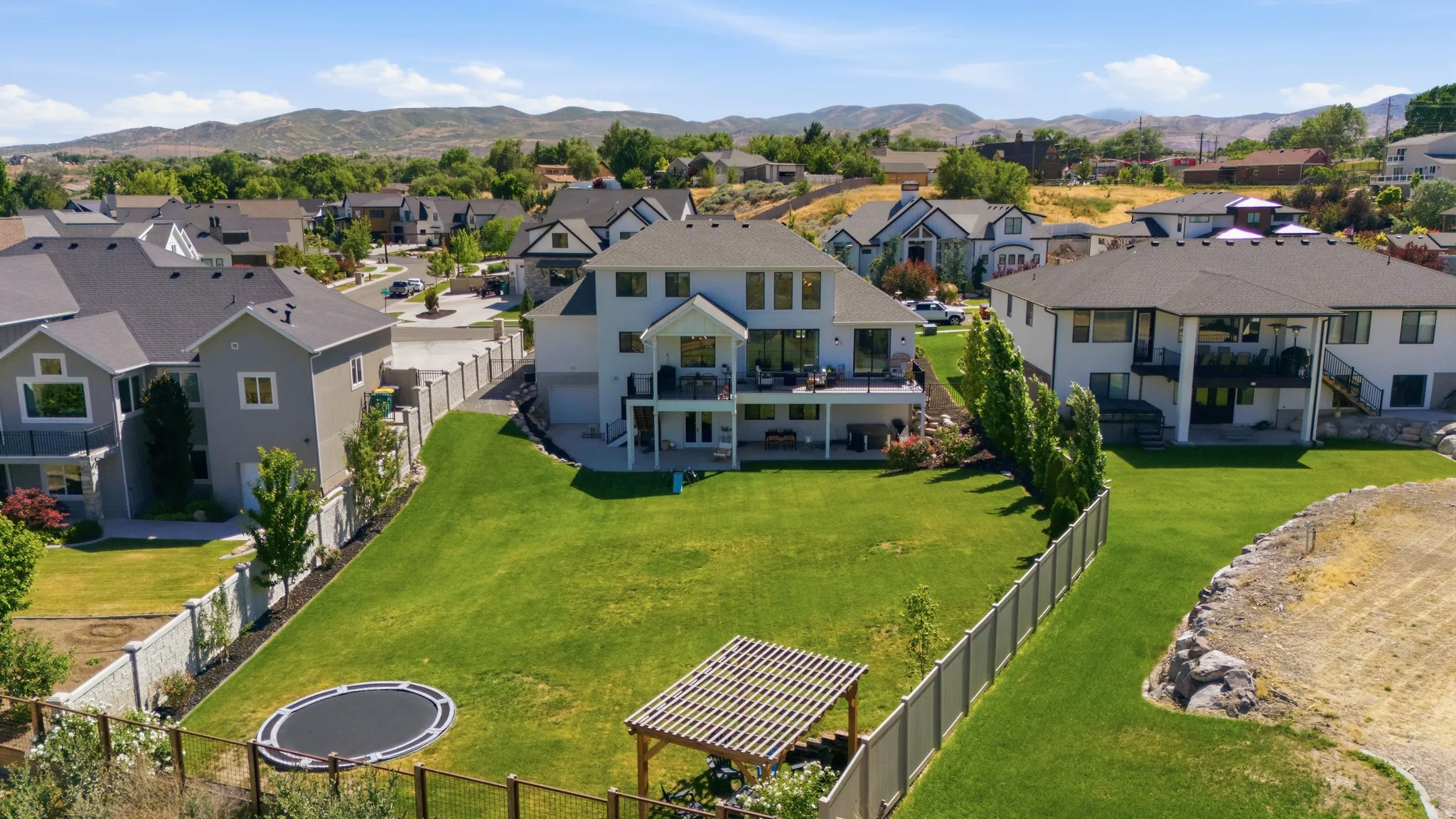 Expansive backyard featuring a lush lawn, two levels of outdoor living space, and mature perimeter trees