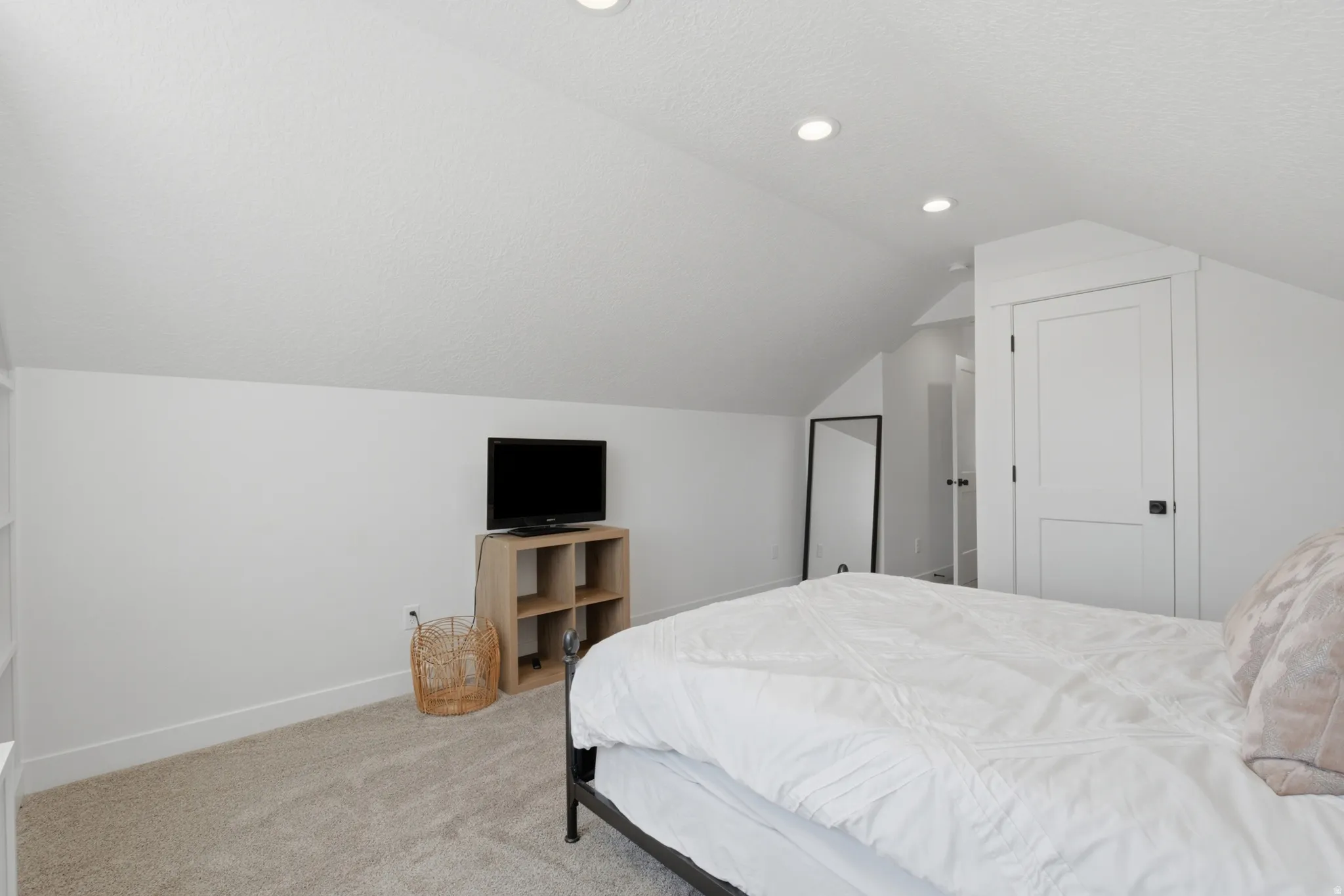 Carpeted room featuring a vaulted ceiling with recessed lighting, white walls, and a white paneled door with matte black hardware